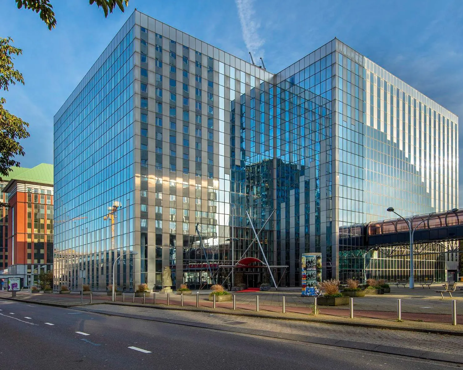 Glazen kantoorgebouw TNW met moderne architectuur en loopbrug in een stedelijke omgeving.