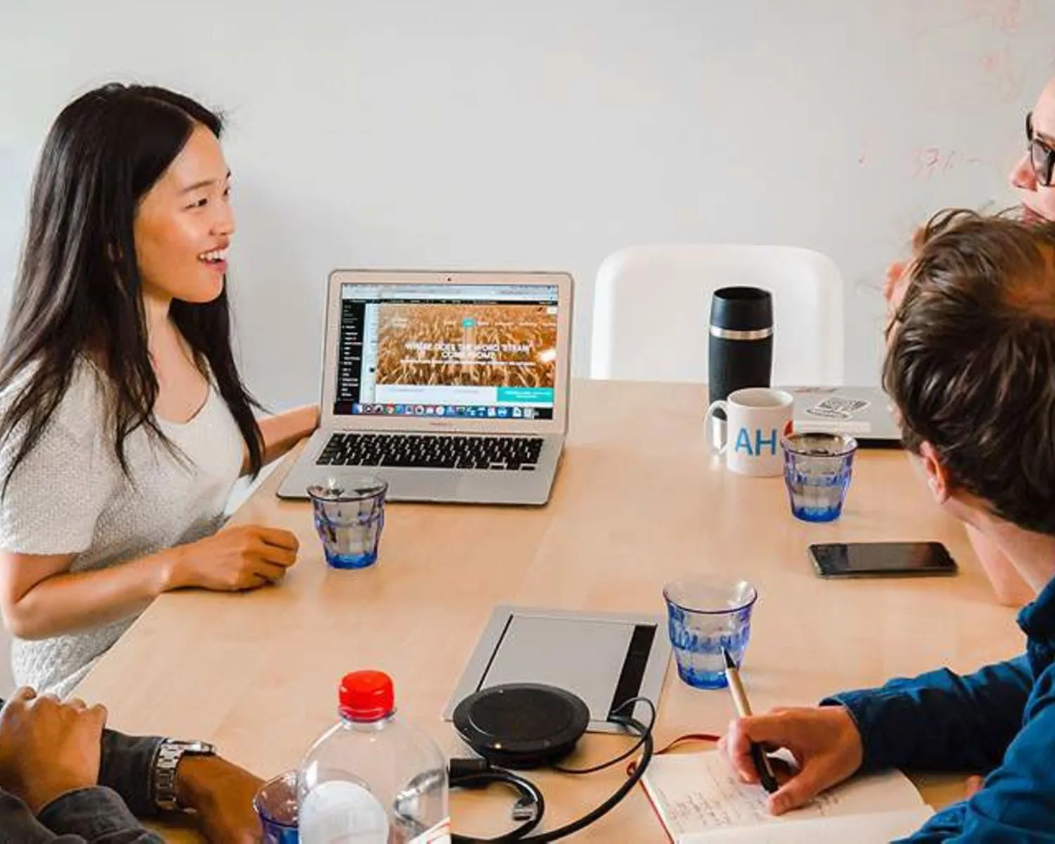 Vier mensen overleggen in een moderne kantoorruimte rond een tafel met een open laptop.