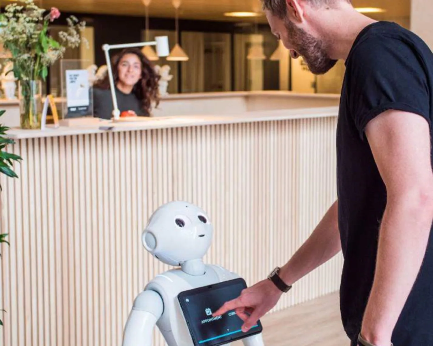 Man bedient een robot-assistent met touchscreen bij de receptie van een moderne kantoorruimte bij TNW.