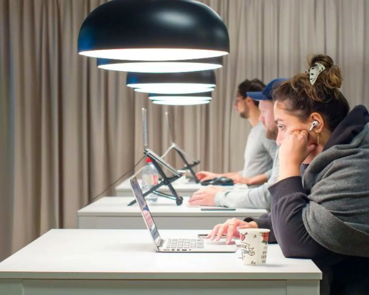 Mensen werken geconcentreerd op laptops in een moderne kantoorruimte van TNW met hanglampen en een rustige uitstraling.