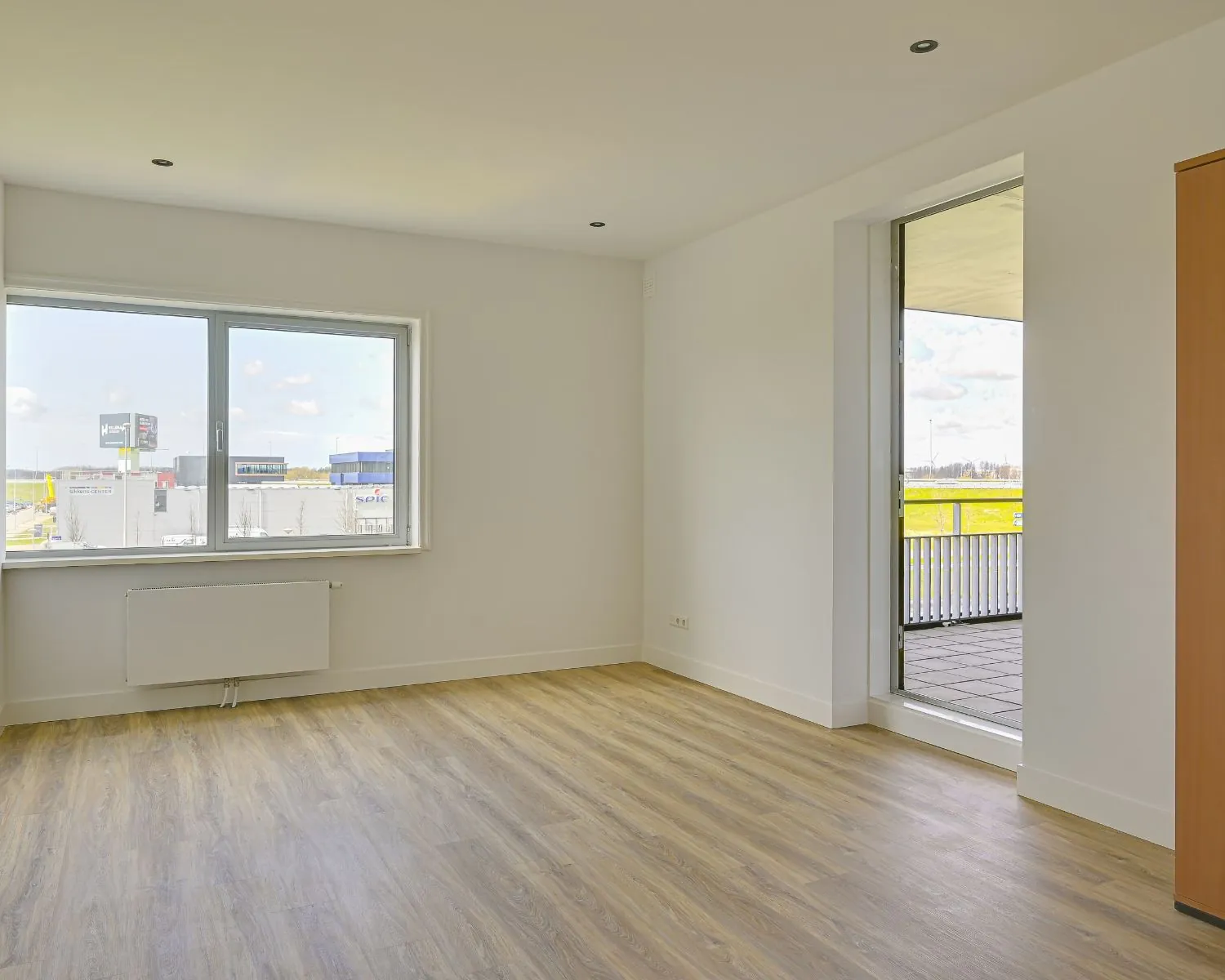 Lichte, moderne kantoorruimte met houten vloer, groot raam en deur naar balkon in Tijnmuiden 89, Amsterdam.