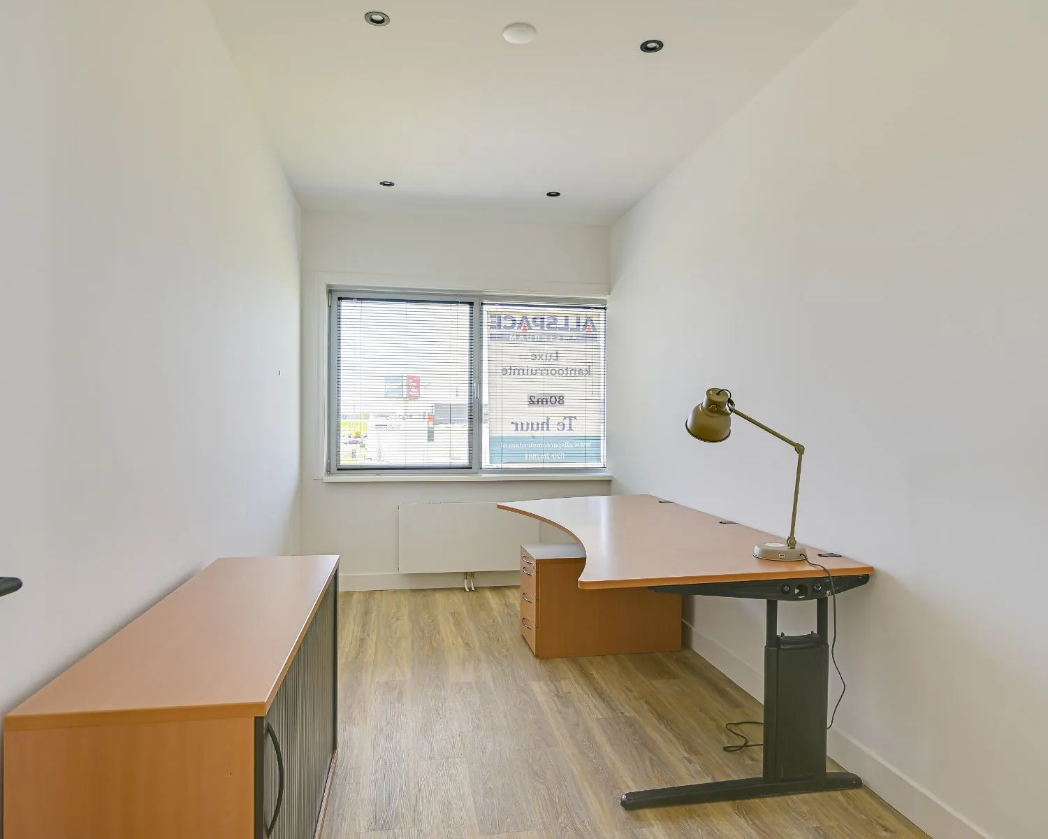 Kleine, moderne kantoorruimte met houten vloer, bureau en raam aan de Tijnmuiden 89 in Amsterdam.