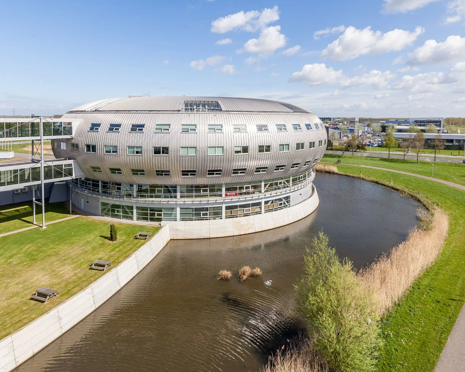 Modern kantoorgebouw Veluwezoom 5 in Almere met ovale vorm, omringd door water en groen.