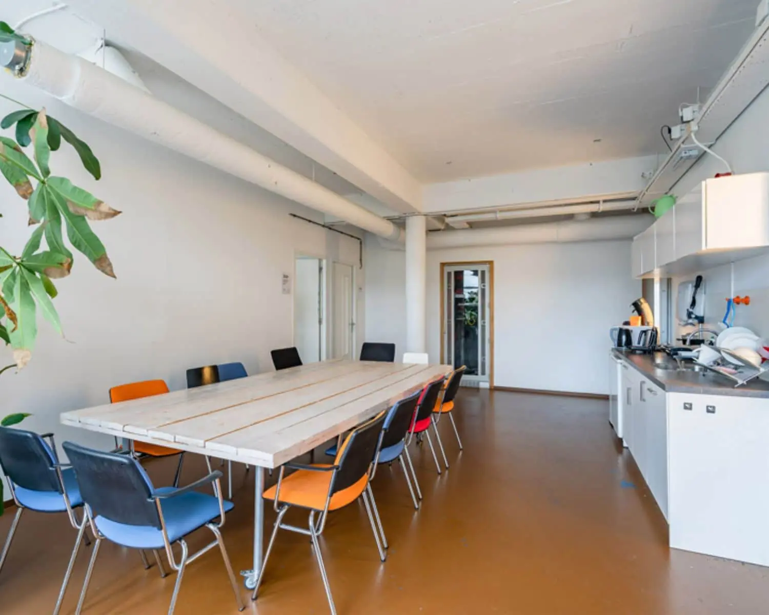 Kantoorruimte met lange vergadertafel, kleurrijke stoelen en keukenblok aan de Vijverhofstraat 47 in Rotterdam.