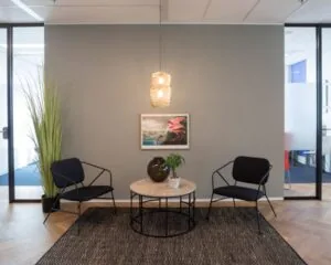 Moderne wachtruimte in kantoor aan de Weena 690 in Rotterdam met twee stoelen, een ronde tafel en wanddecoratie.