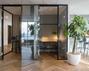 Moderne kantoorruimte met glazen wanden, houten visgraatvloer en grote kamerplant aan de Weena 690 in Rotterdam.