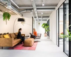 Moderne kantoorruimte aan de Westblaak 90 in Rotterdam met twee vrouwen in gesprek op een bruine bank in een stijlvolle loungehoek.