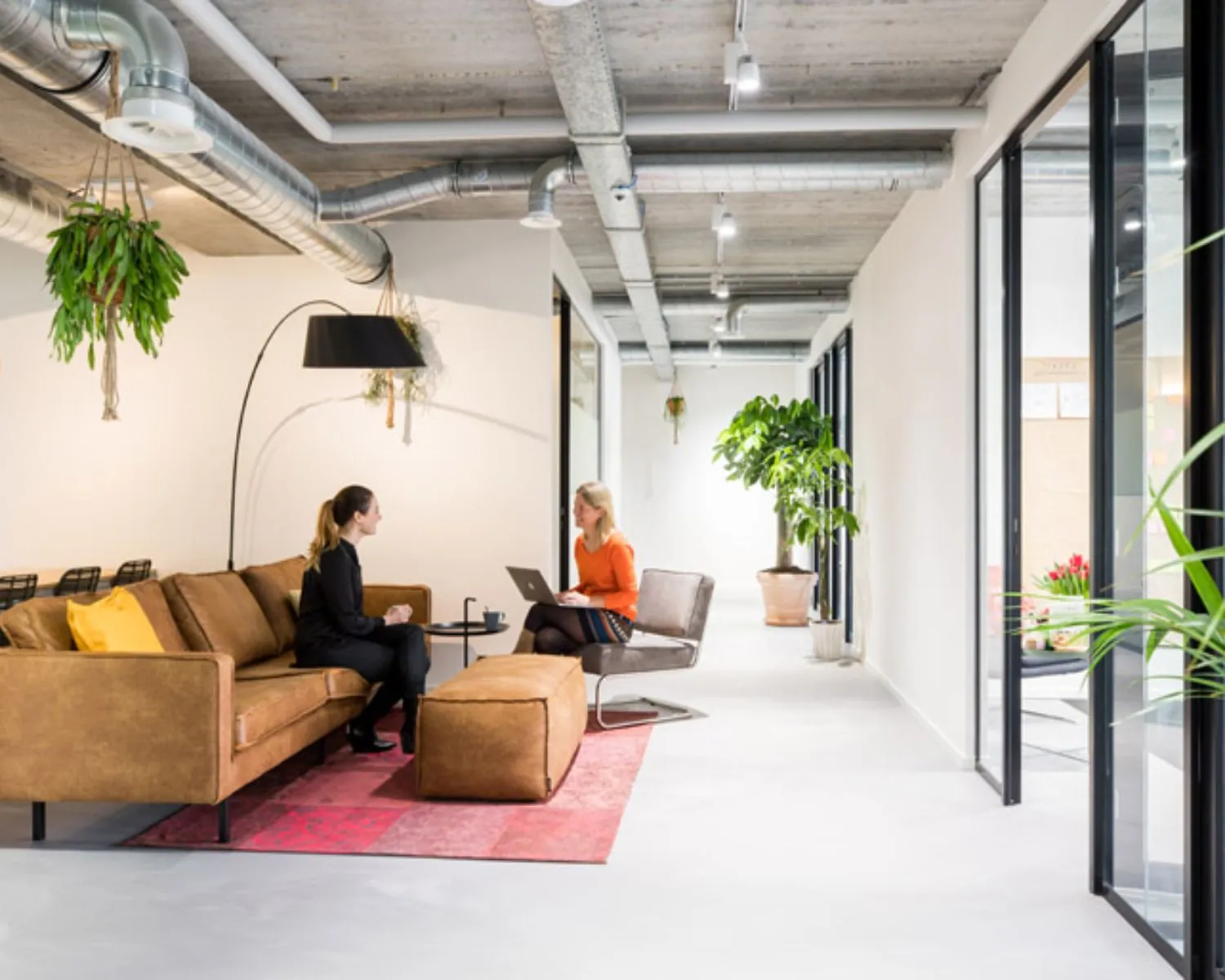 Moderne kantoorruimte aan de Westblaak 90 in Rotterdam met twee vrouwen in gesprek op een bruine bank in een stijlvolle loungehoek.