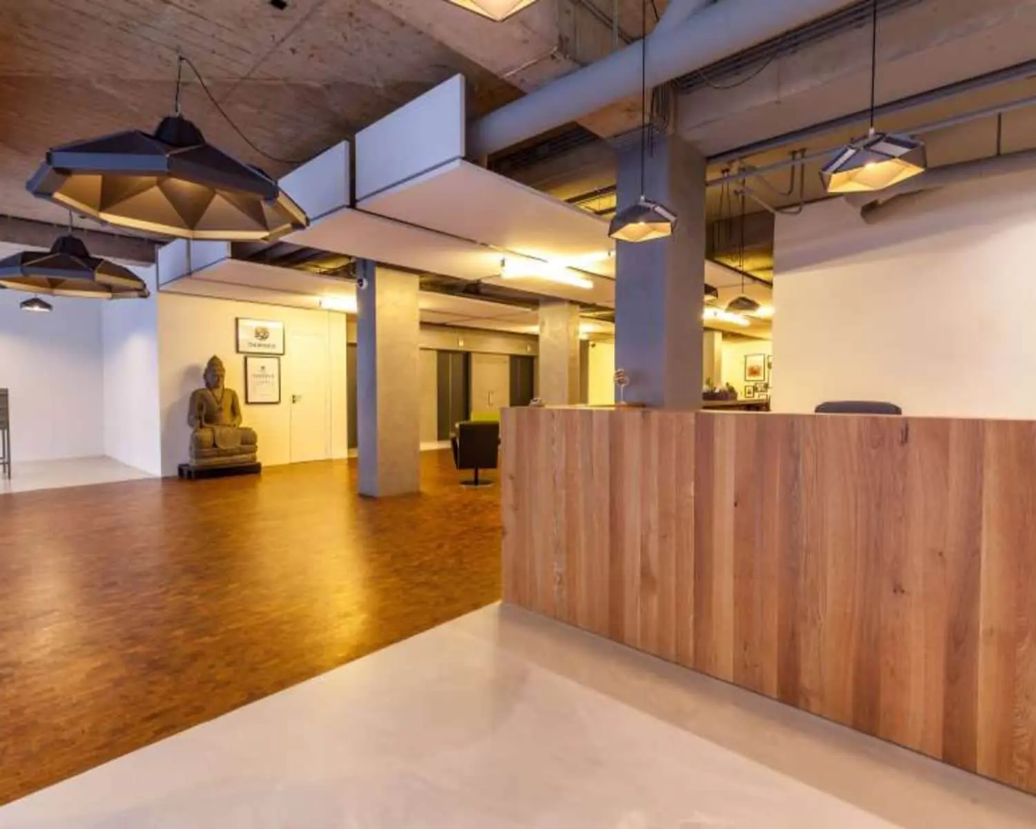 Moderne kantoorruimte aan de Westblaak 90 in Rotterdam met houten receptiebalie, industriële plafondafwerking en een Boeddhabeeld in de hoek.