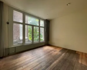 Lichte, lege kantoorruimte met houten vloer en een groot raam aan de Weteringschans 130 in Amsterdam.