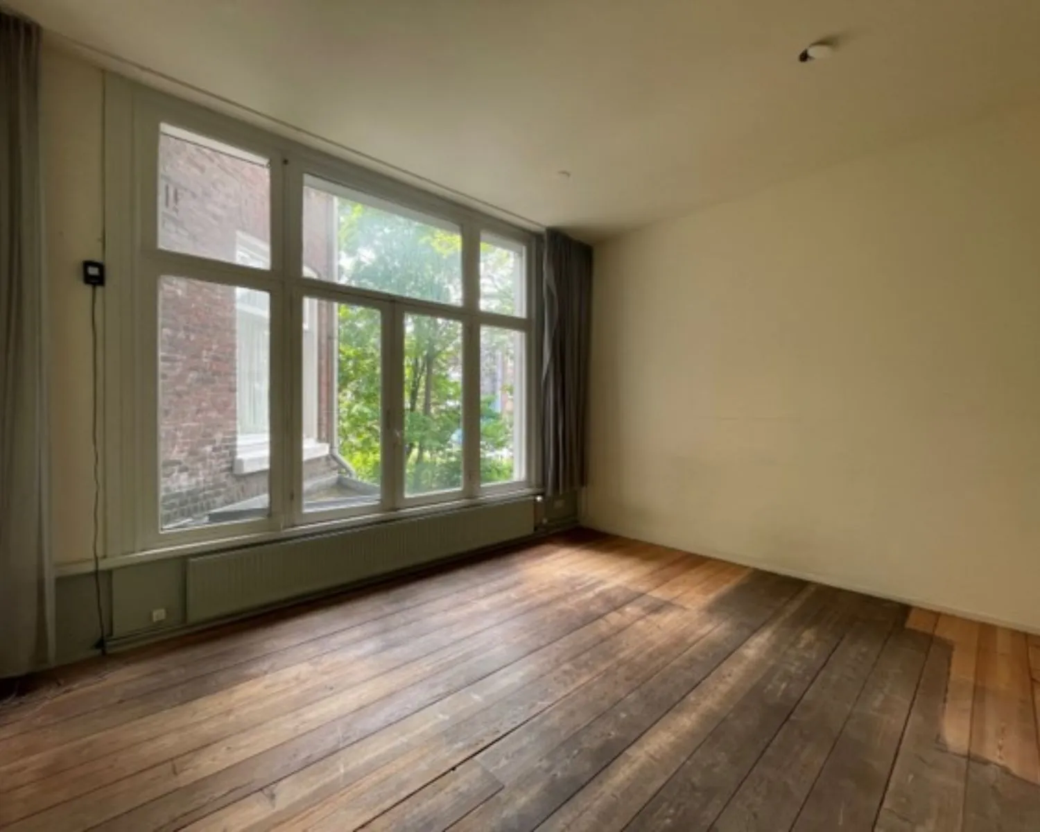 Lichte, lege kantoorruimte met houten vloer en een groot raam aan de Weteringschans 130 in Amsterdam.