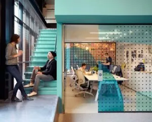 Moderne kantoorruimte aan de Wibautstraat 131 met glazen vergaderruimte en werknemers in gesprek op een turquoise trap.