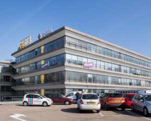 Modern kantoorpand aan het Winschoterdiep 50 in Groningen met diverse bedrijfslogo’s en een parkeerplaats op de voorgrond.