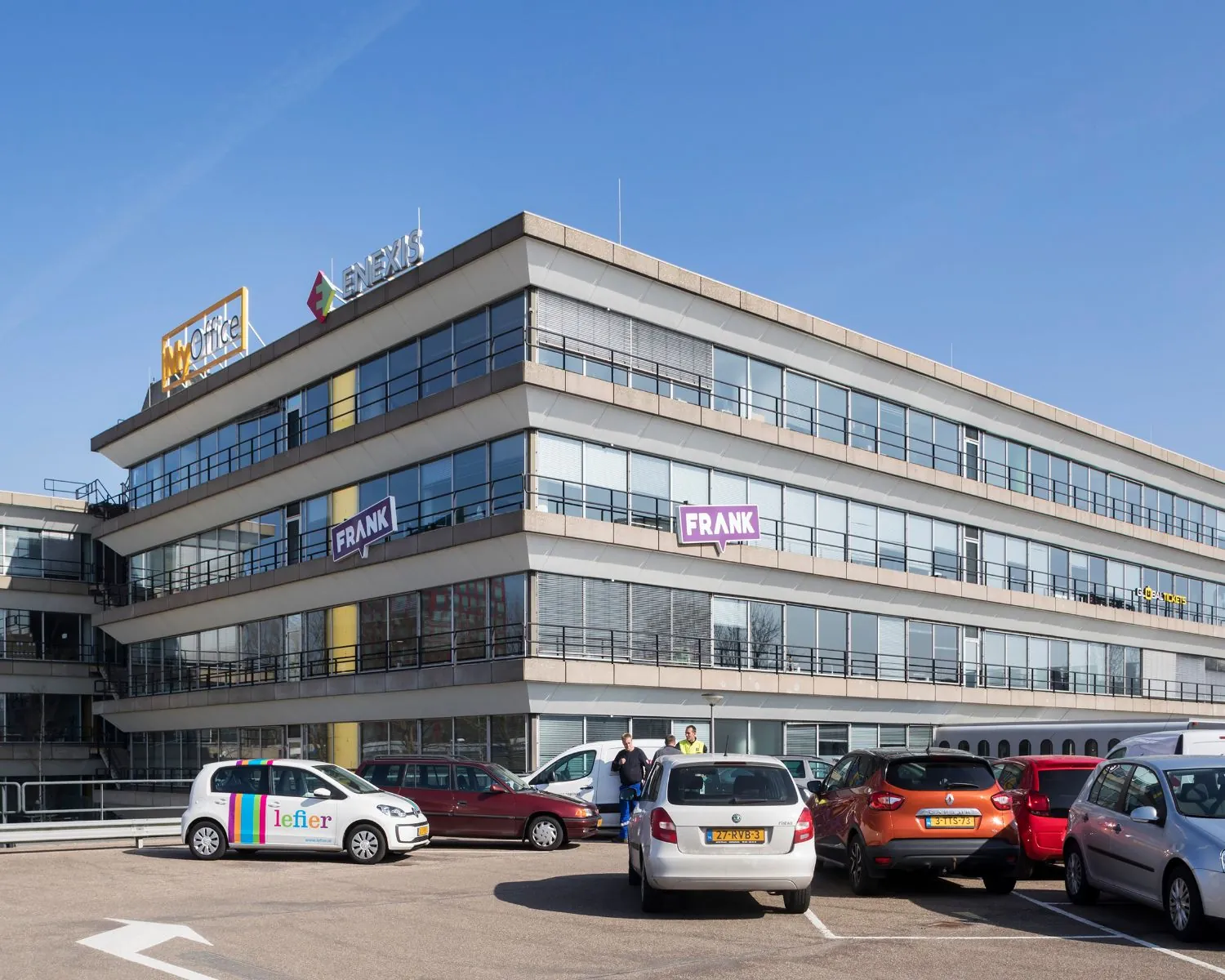 Modern kantoorpand aan het Winschoterdiep 50 in Groningen met diverse bedrijfslogo’s en een parkeerplaats op de voorgrond.