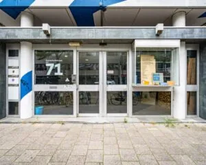 Ingang van het kantoorpand aan de Zomerhofstraat 71 in Rotterdam met glazen deuren en fietsenstalling op de achtergrond.