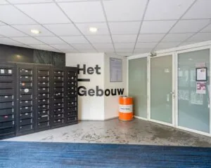 Ingangshal van Het Gebouw aan de Zomerhofstraat 71 in Rotterdam met zwarte postvakken, een oranje afvalbak en witte glazen deuren.