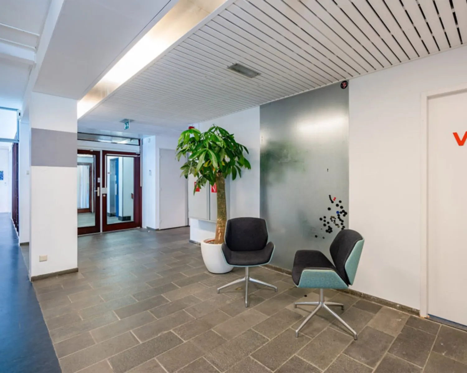 Moderne entreehal van een kantoorpand aan de Zomerhofstraat 84 in Rotterdam met twee stoelen, een plant en grijze tegelvloer.