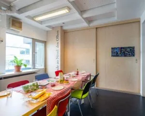 Vergaderruimte met lange tafel, kleurrijke stoelen en een gedekte tafel in kantoor aan de Zomerhofstraat 84 in Rotterdam.