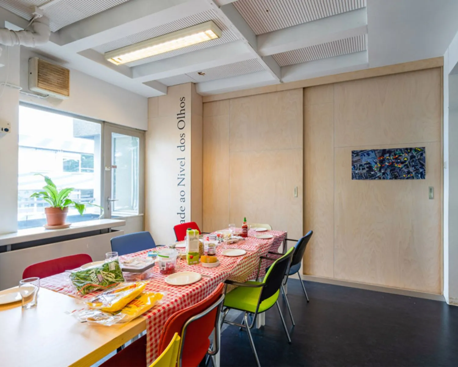 Vergaderruimte met lange tafel, kleurrijke stoelen en een gedekte tafel in kantoor aan de Zomerhofstraat 84 in Rotterdam.