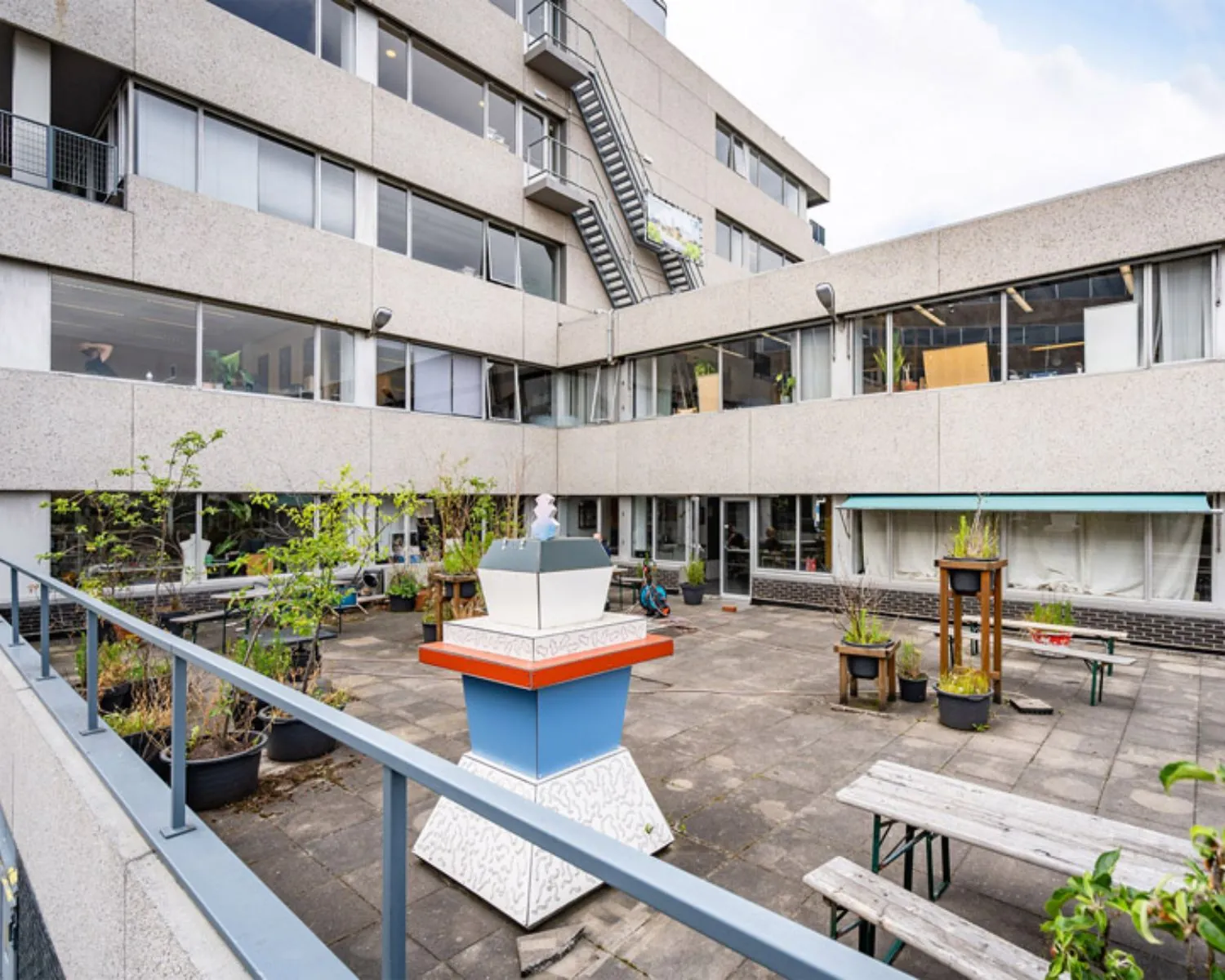 Binnenplein van kantoorpand aan de Zomerhofstraat 84 in Rotterdam met zitbanken, plantenbakken en kunstobject.