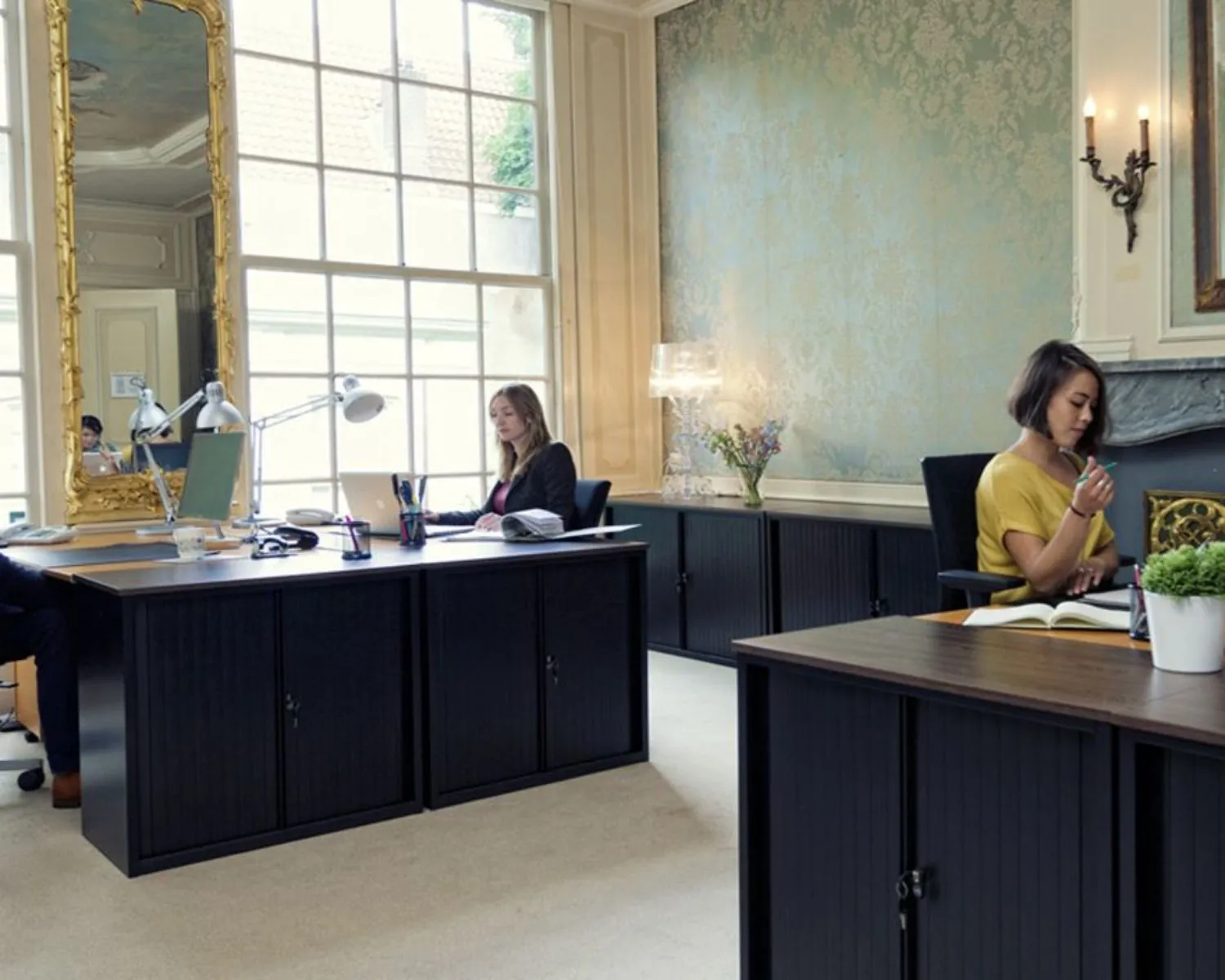 Stijlvolle kantoorruimte aan de Keizersgracht met grote ramen, klassieke details en werkende mensen aan bureaus.