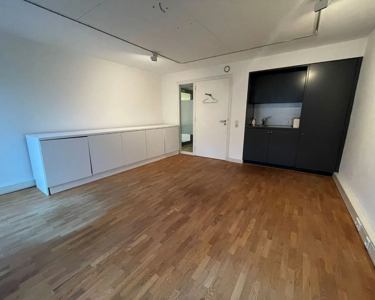 Lege kantoorruimte met houten vloer, ingebouwde witte kasten en een compacte kitchenette aan de Nieuwe Herengracht 51 in Amsterdam.