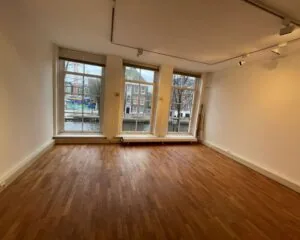 Lichte kantoorruimte met houten vloer en grote ramen met uitzicht op de gracht aan de Nieuwe Herengracht 51 in Amsterdam.