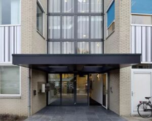 Ingang van een modern kantoorgebouw aan de Regulierenring 2 in Bunnik met glazen deuren en overkapping.
