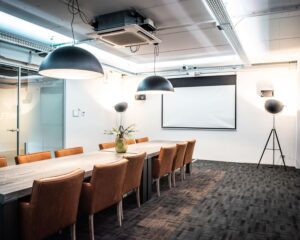 Moderne vergaderruimte aan de Van Cleeffkade met lange tafel, leren stoelen en een projector.