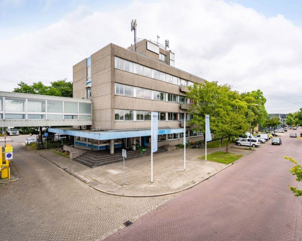 Vooraanzicht van een kantoorgebouw aan de Van Heekstraat 15 in Schiedam met parkeerplaatsen en vlaggenmasten.