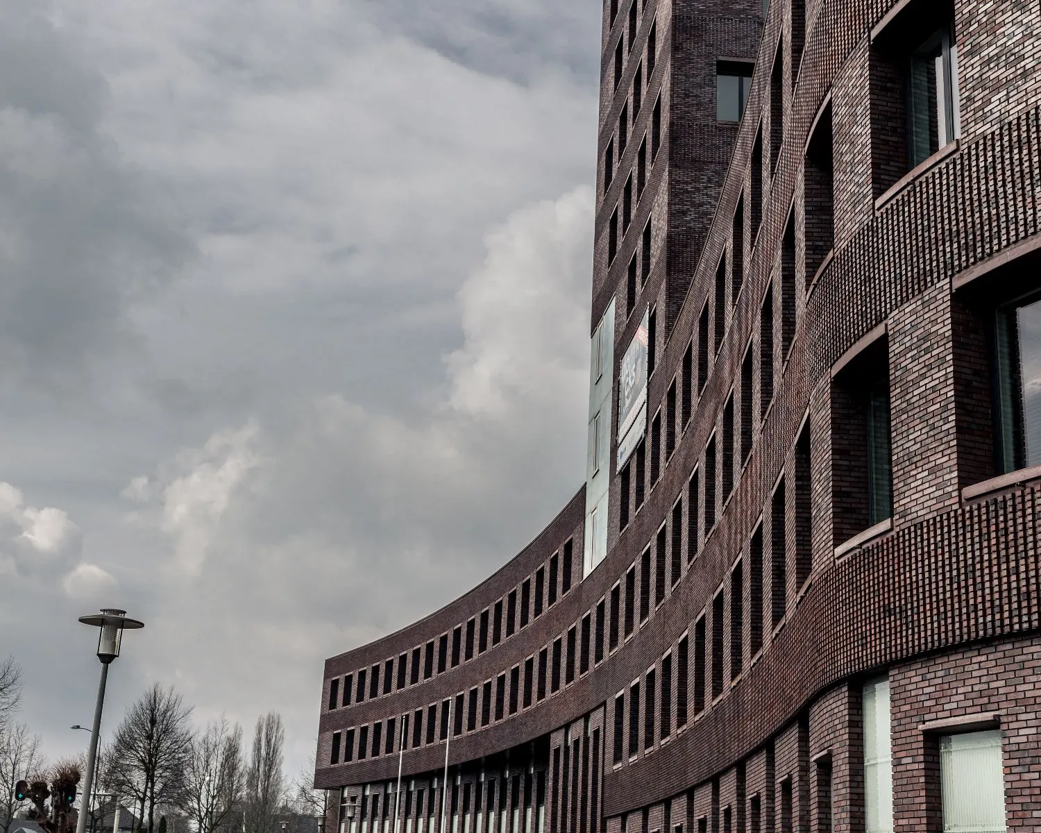 Gebogen, modern kantoorgebouw aan de Wapenrustlaan 11-31 in Apeldoorn tegen een bewolkte lucht.