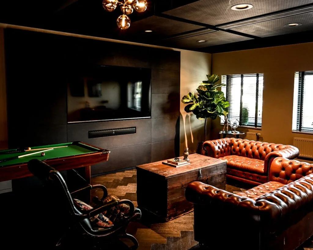 Stijlvol ingerichte kantoorruimte aan de Wapenrustlaan in Apeldoorn met leren chesterfieldbanken, een houten salontafel, een televisie en een pooltafel.