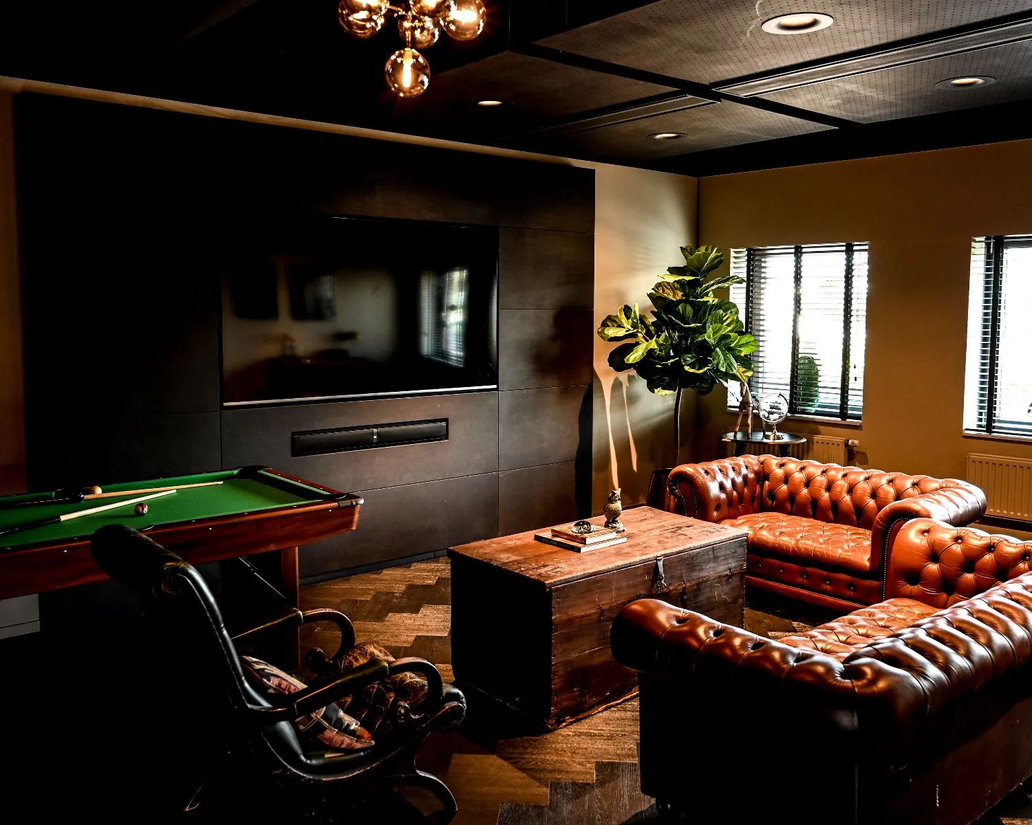 Stijlvol ingerichte kantoorruimte aan de Wapenrustlaan in Apeldoorn met leren chesterfieldbanken, een houten salontafel, een televisie en een pooltafel.