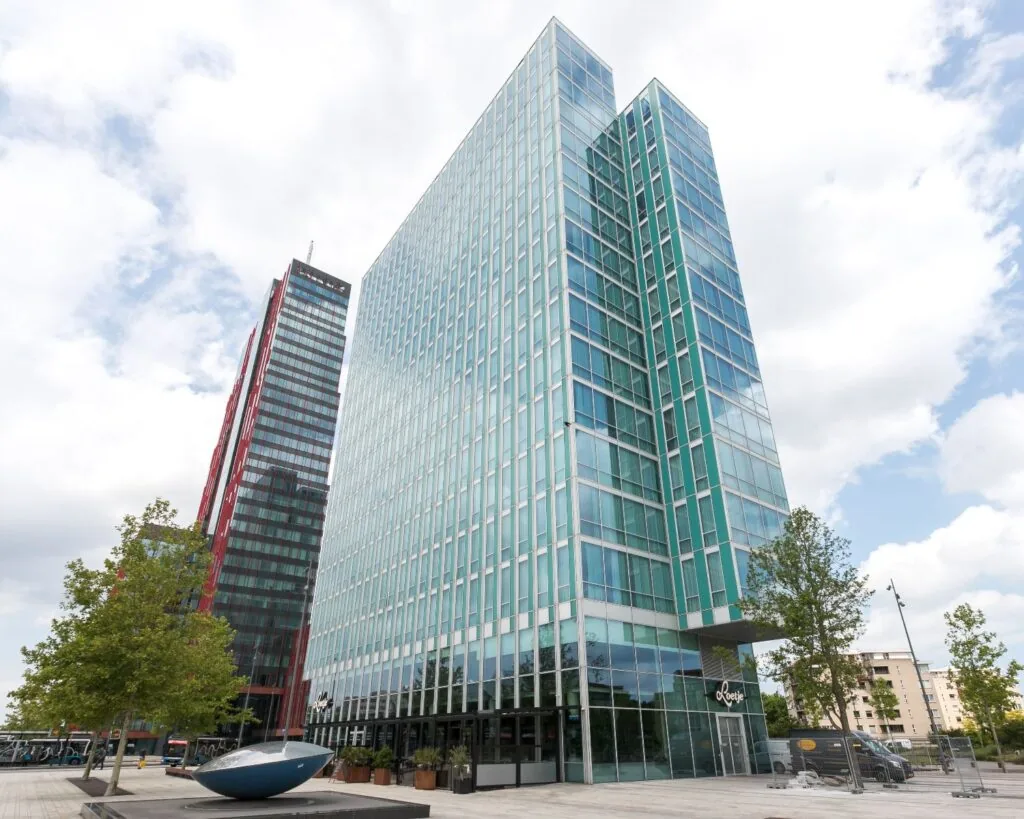 Moderne kantoortorens aan het Mandela Plein in Almere met glasgevels en omliggende stedelijke omgeving.