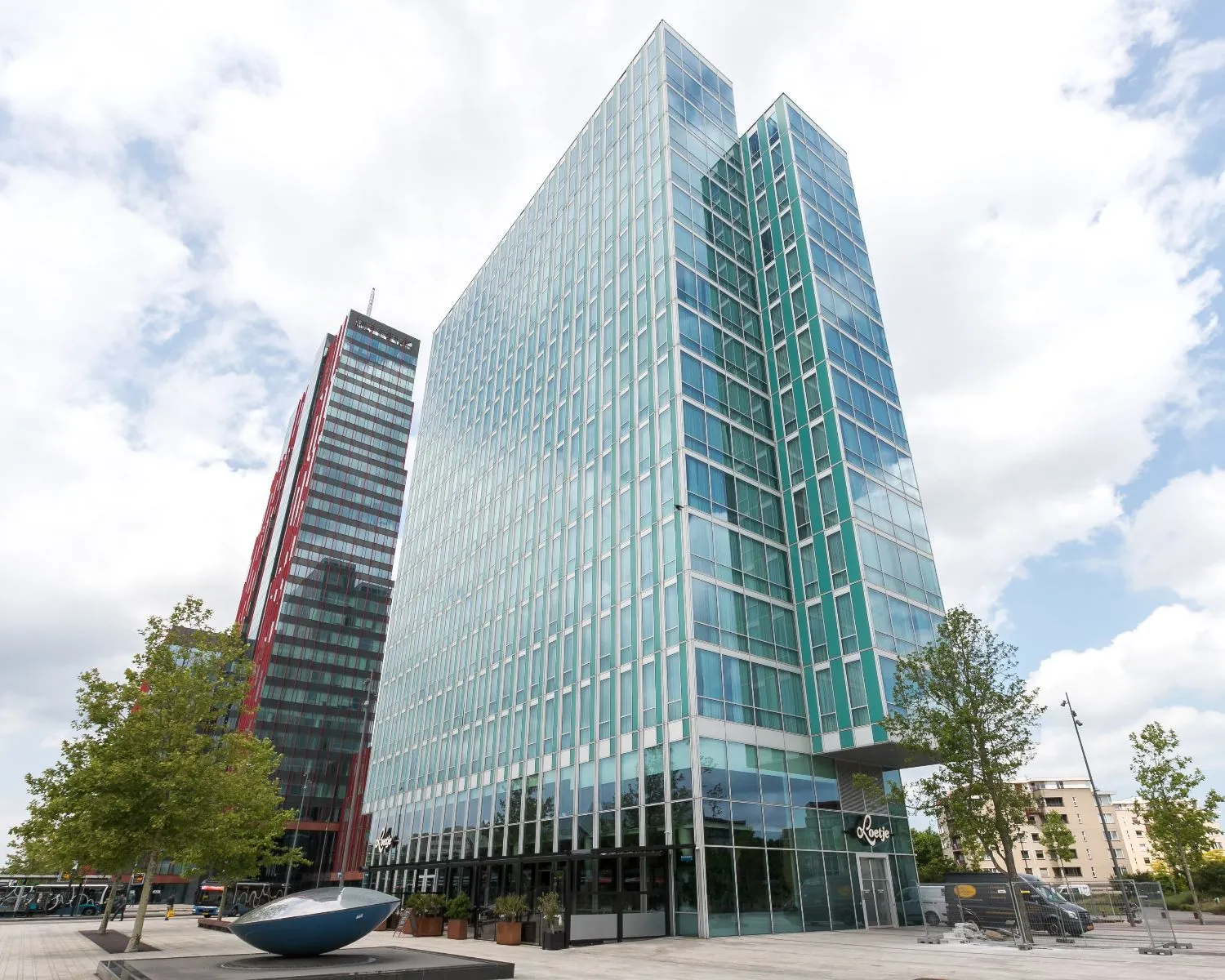 Moderne kantoortorens aan het Mandela Plein in Almere met glasgevels en omliggende stedelijke omgeving.