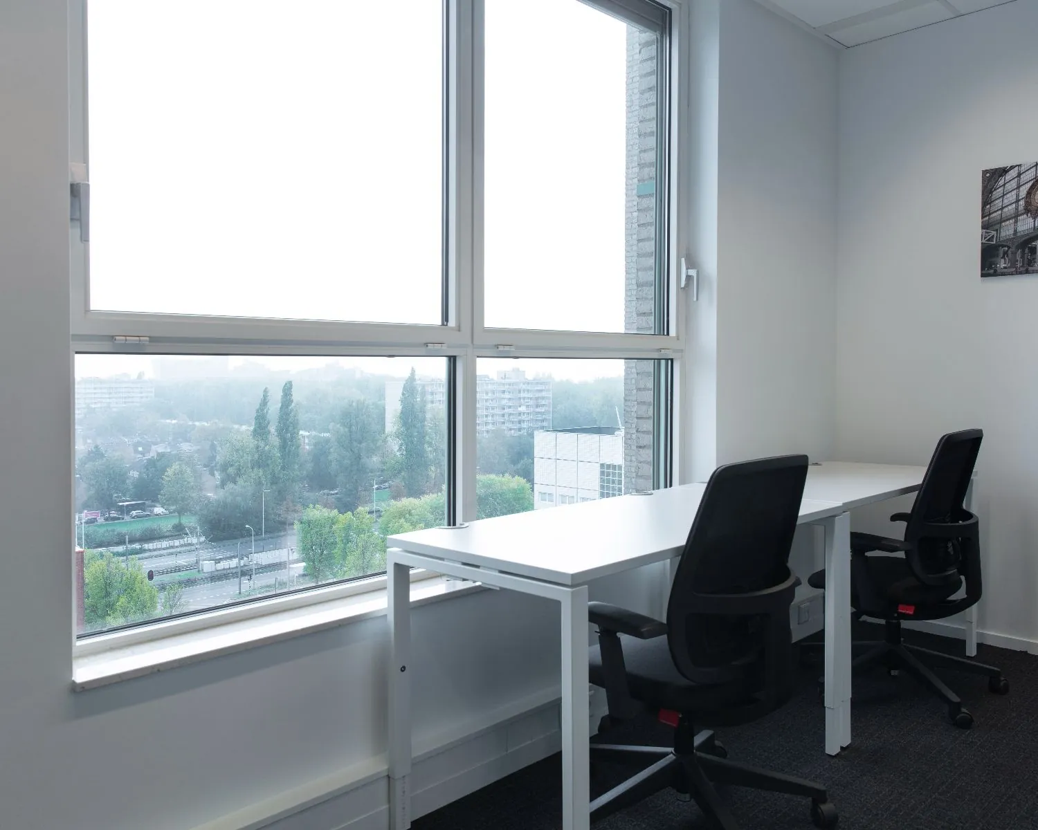 Twee werkplekken met bureaus en bureaustoelen in een lichte kantoorruimte in Amstelveen met uitzicht op de stad.
