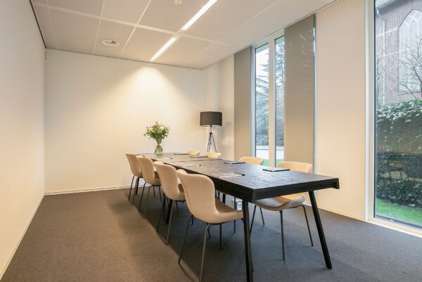 Moderne vergaderruimte met lange tafel, acht stoelen en grote ramen in kantoor aan de Cuserstraat 91 in Amsterdam.