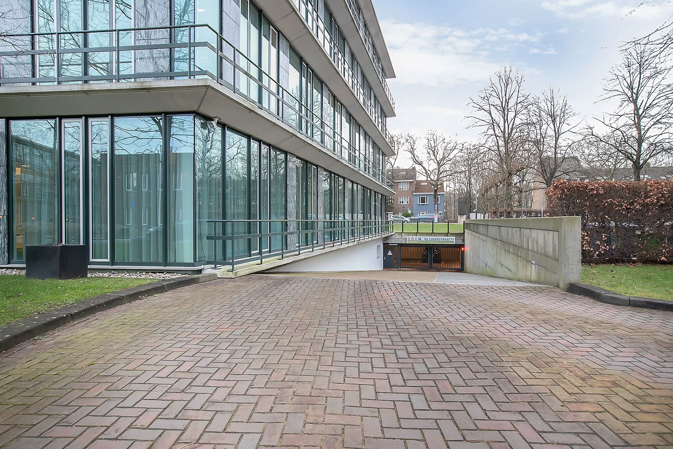 Ingang van de parkeergarage en glazen gevel van een kantoorgebouw aan de Cuserstraat 91 in Amsterdam.