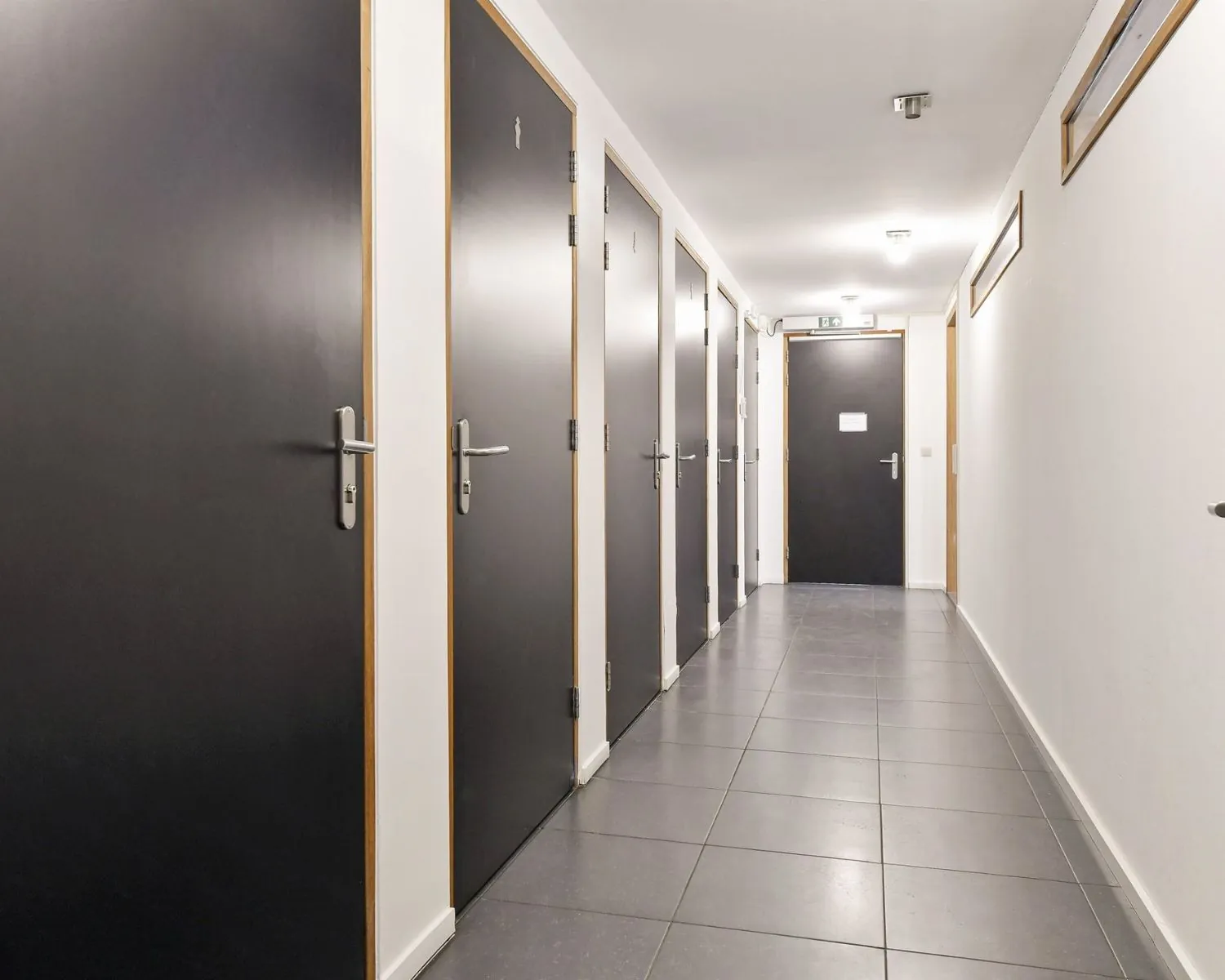 Verlichte gang met meerdere zwarte deuren in een kantoorgebouw aan de Asterweg 20F in Amsterdam.