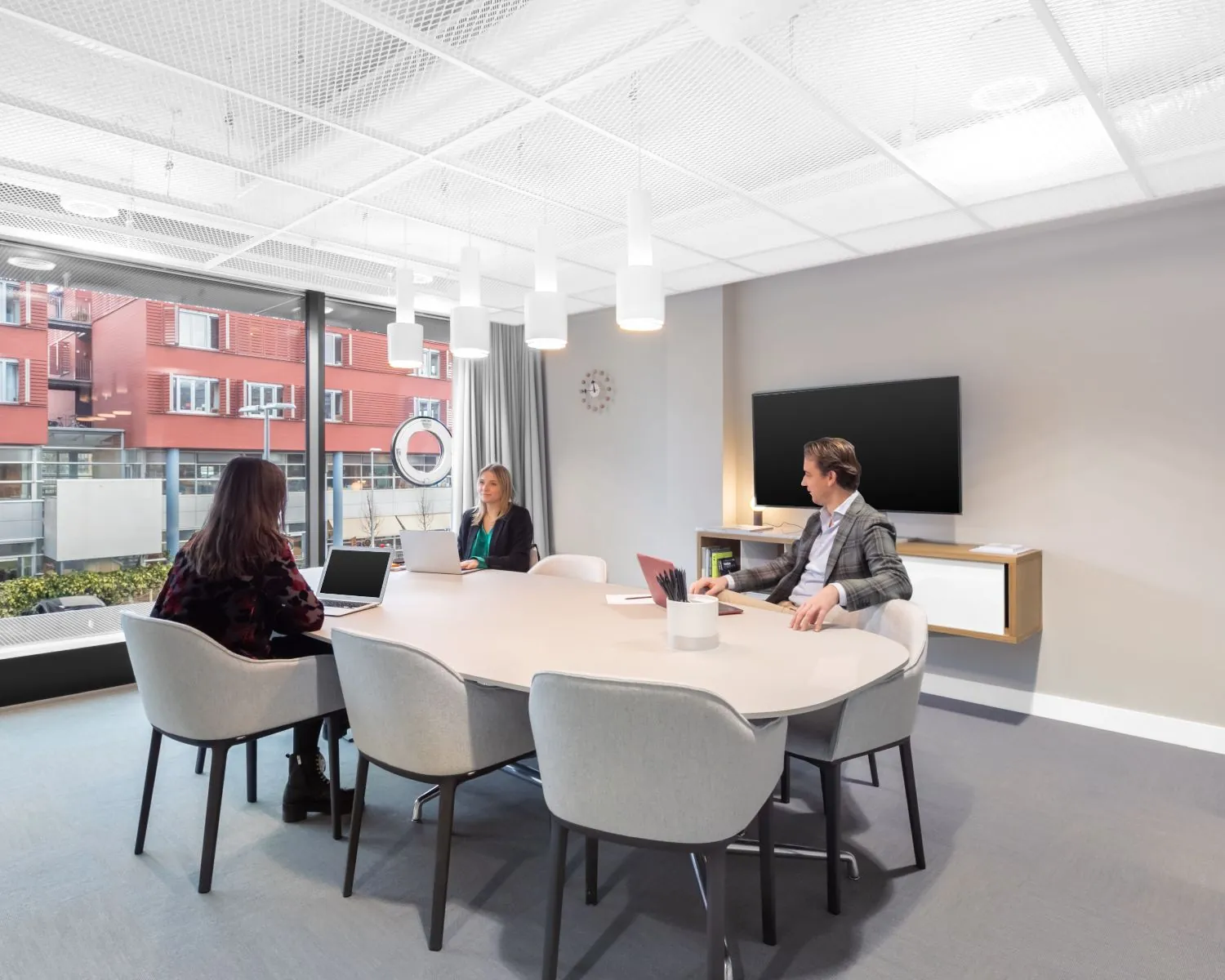 Moderne vergaderruimte in kantoorpand De Walvis in Amsterdam met drie mensen aan een ovale tafel.