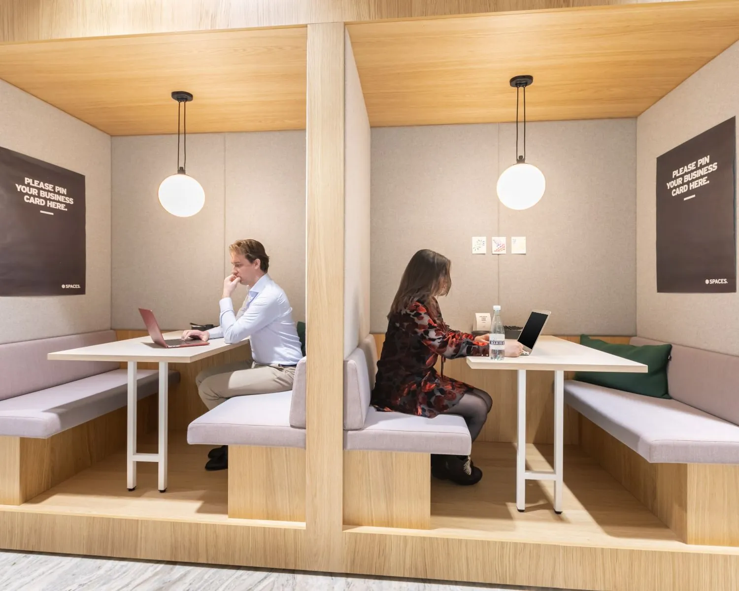 Twee mensen werken afzonderlijk op laptops in moderne werkpods in kantoorgebouw De Walvis aan de Grote Bickersstraat in Amsterdam.