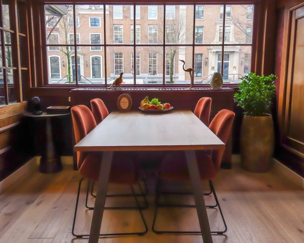 Moderne vergaderruimte aan de Herengracht in Amsterdam met houten tafel, rode stoelen en uitzicht op karakteristieke grachtenpanden.