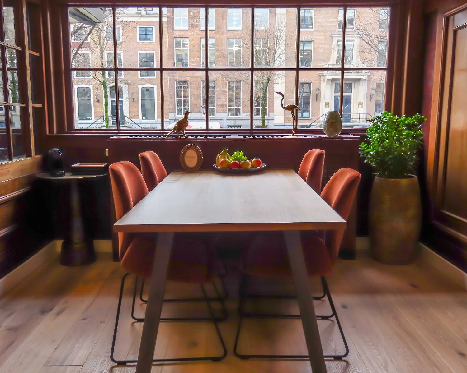 Moderne vergaderruimte aan de Herengracht in Amsterdam met houten tafel, rode stoelen en uitzicht op karakteristieke grachtenpanden.