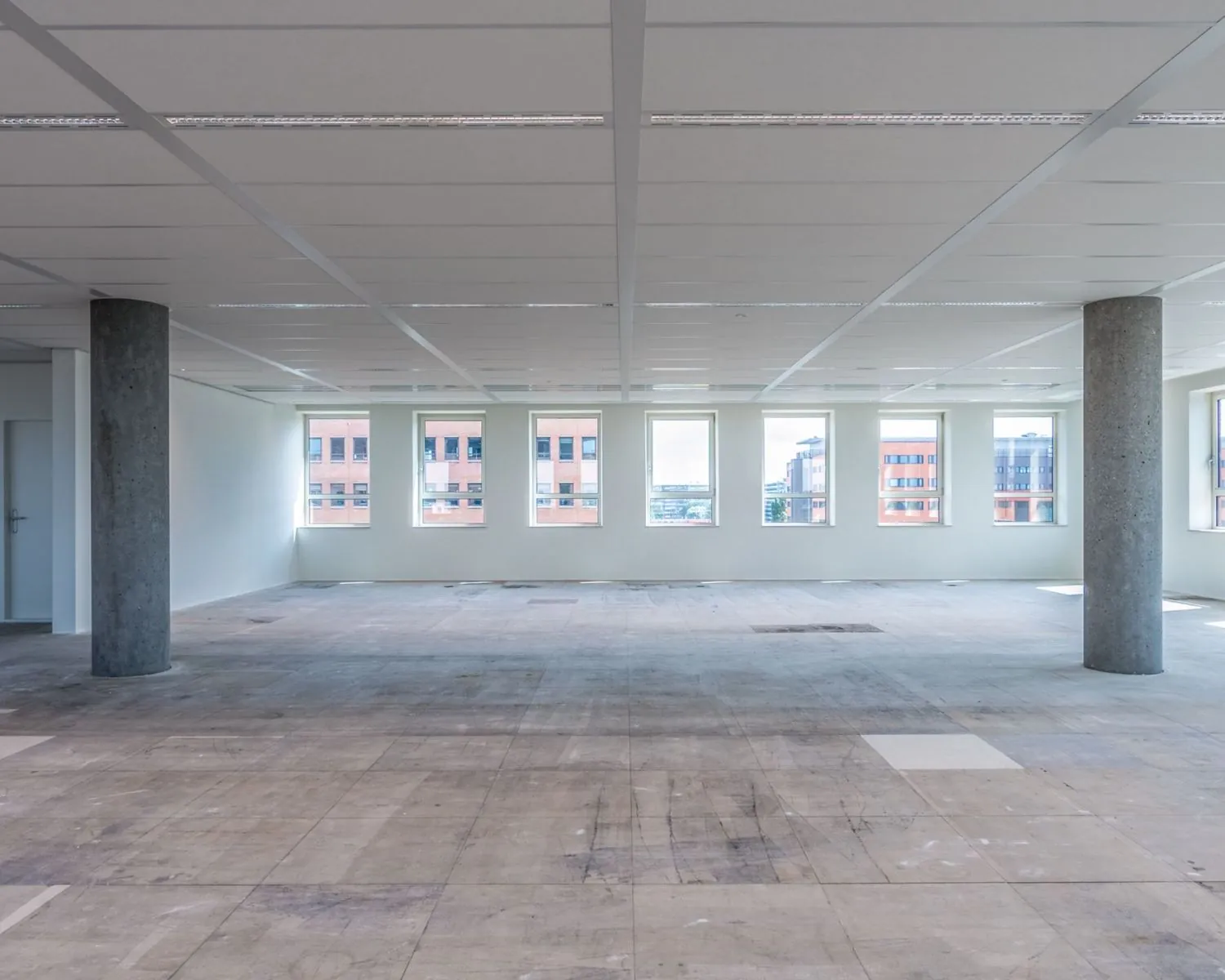 Lege kantoorruimte te huur aan de Hullenbergweg 81 in Amsterdam met grote ramen en betonnen pilaren.
