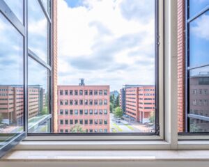 Uitzicht vanuit een geopend raam op meerdere moderne kantoorgebouwen aan de Hullenbergweg in Amsterdam.