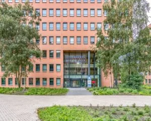 Voorgevel van een modern kantoorgebouw aan de Hullenbergweg 81 in Amsterdam met glazen entree en omliggend groen.