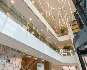 Moderne entreehal van een kantoorgebouw aan de Hullenbergweg 81 in Amsterdam met glazen balustrades, hangende verlichting en binnengroen.