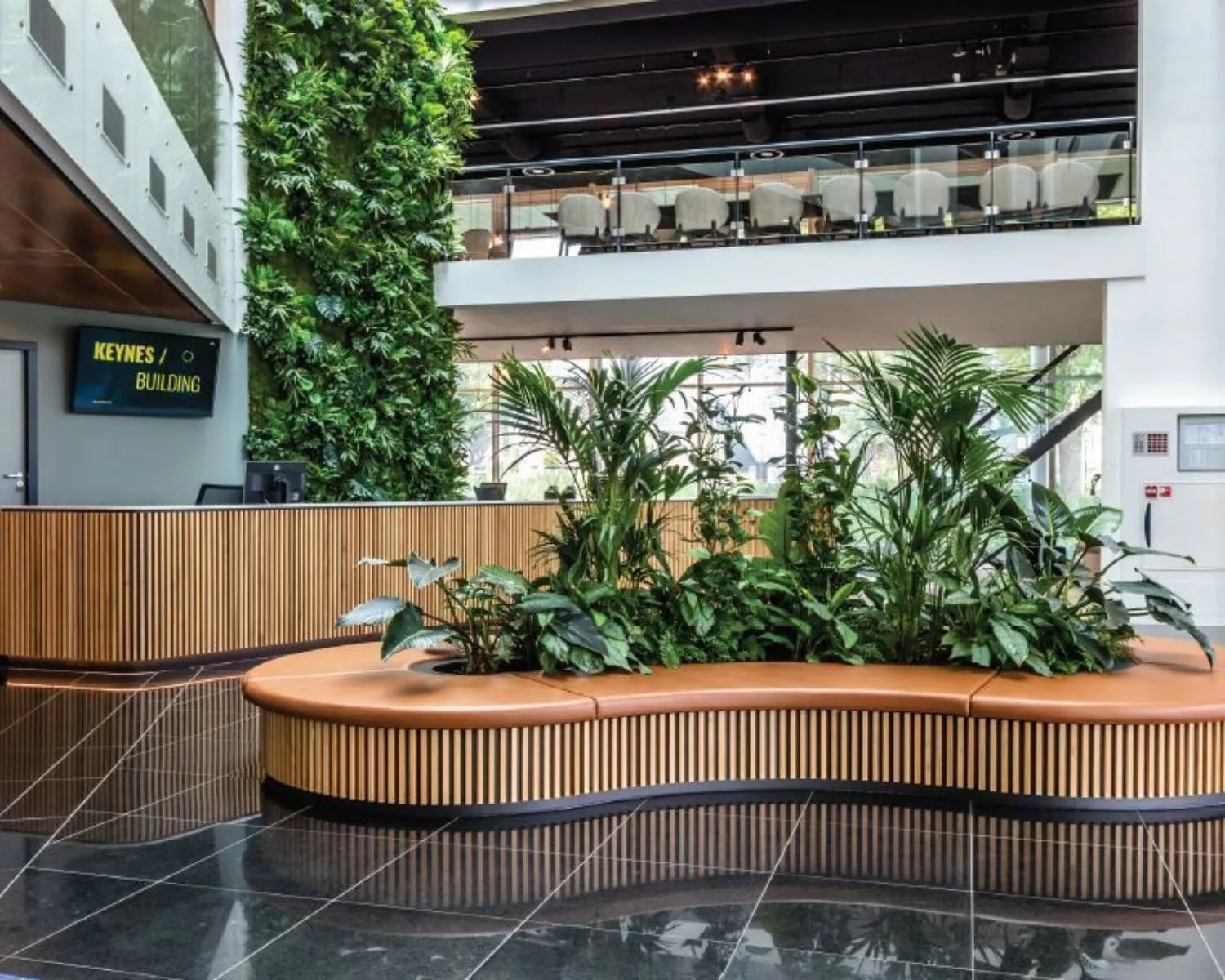 Moderne kantoorlobby in het Keynes Building in Amsterdam met houten balie, groene plantenwand en zitgedeelte met binnentuin.
