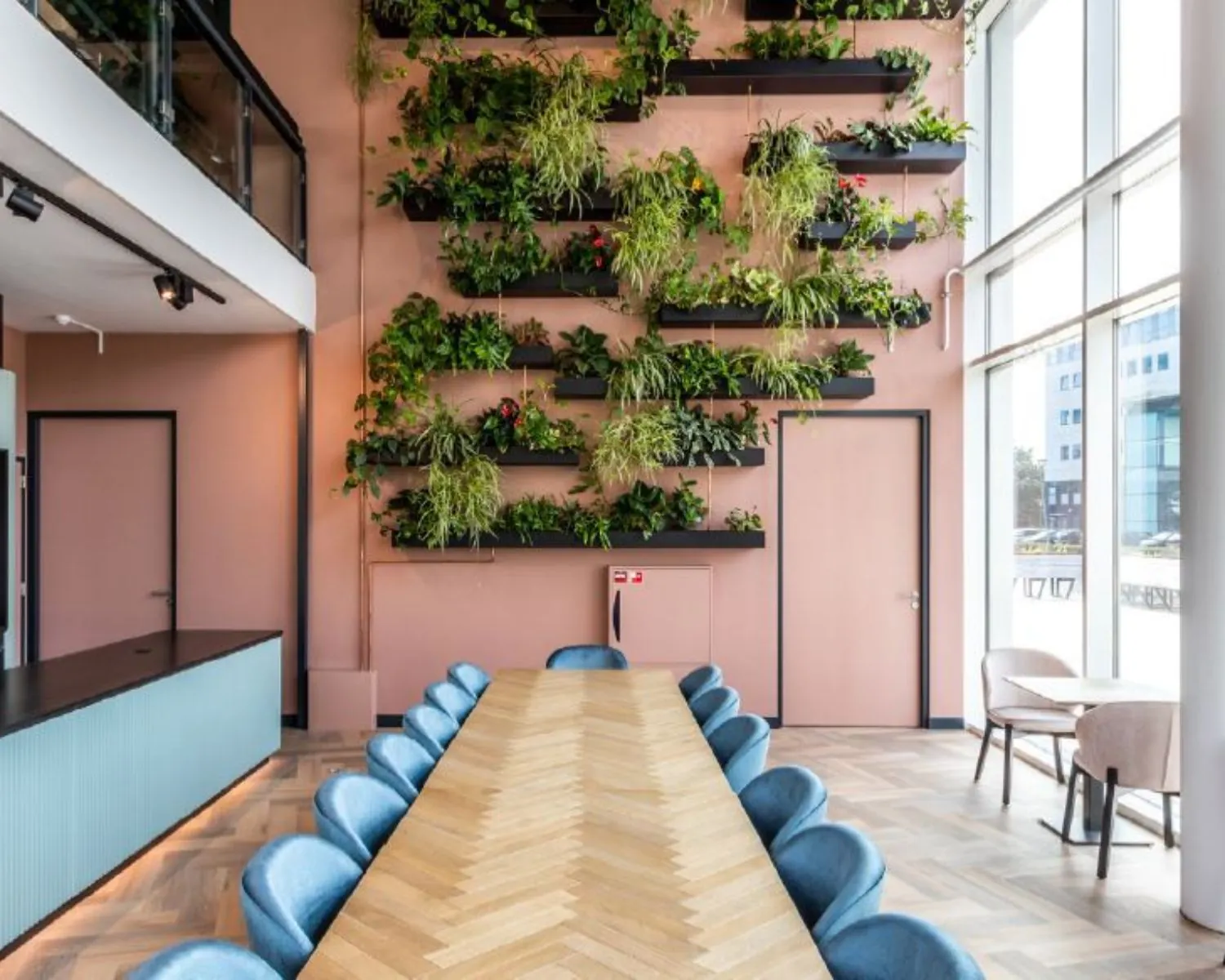 Moderne vergaderruimte op John M. Keynesplein 10 in Amsterdam met een lange houten tafel, blauwe stoelen en een groene plantenwand.
