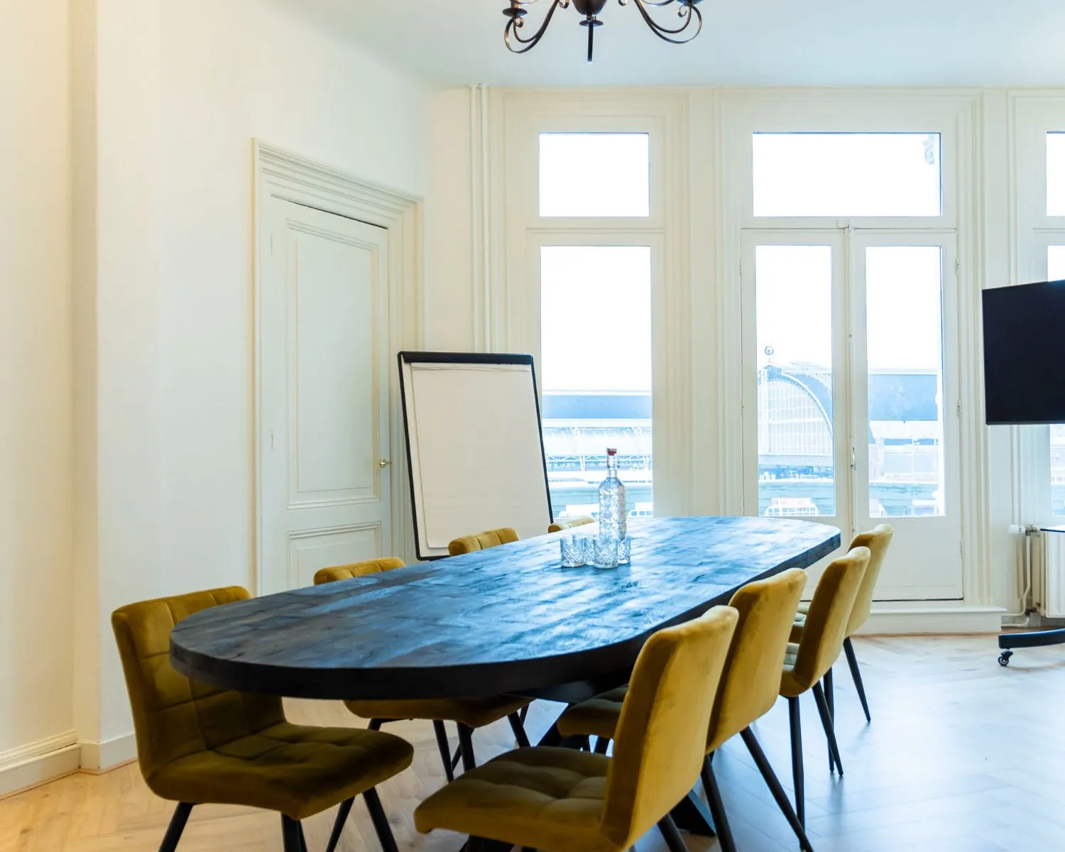 Vergaderruimte met ovale tafel, gele stoelen en uitzicht op Amsterdam Centraal aan de Prins Hendrikkade.